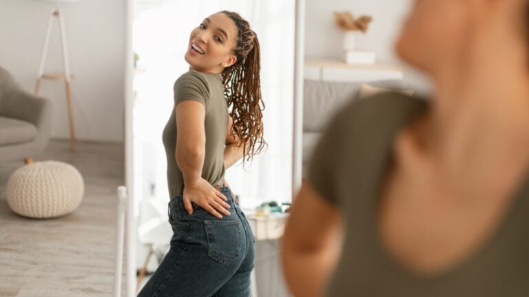 Great Weight Loss. Joyful African American Woman Looking At Her Reflection In Mirror After Successful Slimming And Diet Posing Standing At Home. Beauty And Healthcare Concept. Selective Focus