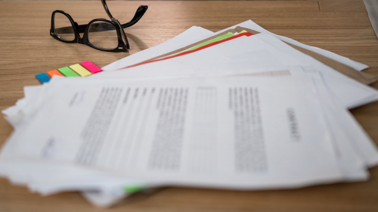 A desk in an office full of necessary documents for work. Next to it there are men's glasses and colored sheets of paper for marking important content. Cabinet for work at home.