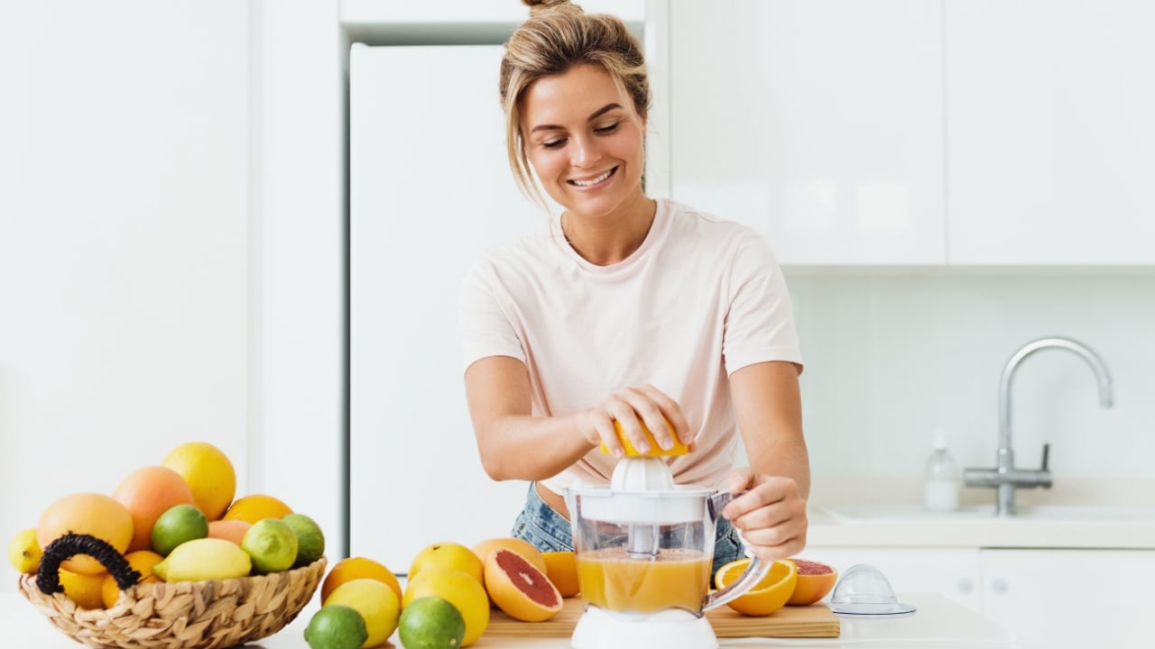 Young cheerful woman with a lot of citrus fruits during fresh orange juice preparation at home