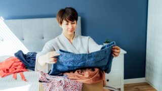 Woman selecting clothes from her wardrobe for donating to a Charity shop. Decluttering, Sorting clothes and Cleaning Up. Reuse, second-hand concept. Conscious consumer, sustainable lifestyle