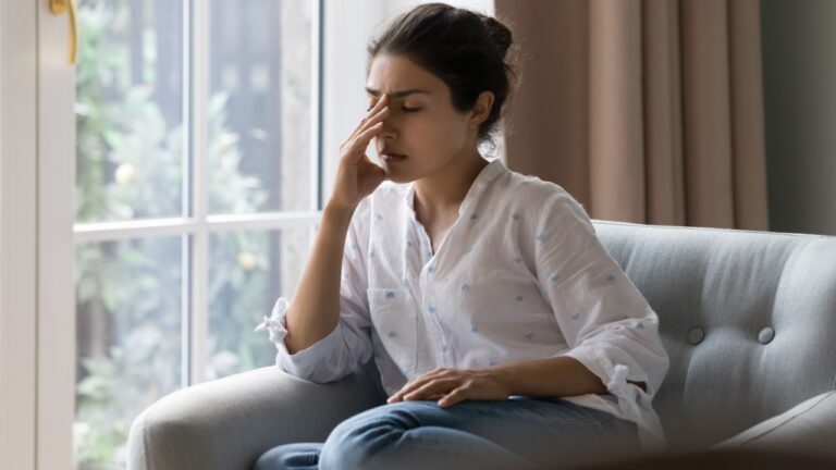 Depressed frustrated young Indian woman suffering from headache, migraine, touching face, head with closed eyes, feeling stressed, sick, tired, thinking over bad news, problems, crisis
