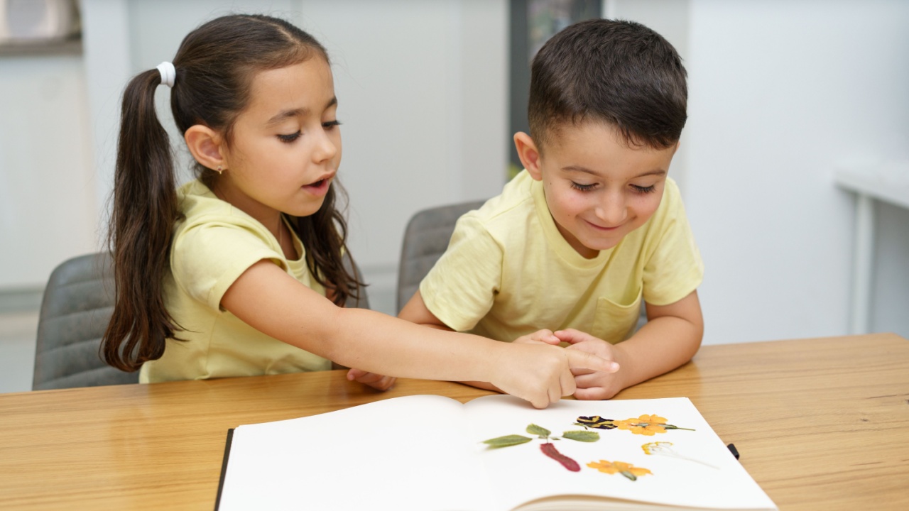 Children making herbarium. Funny kids arranging pressed flowers in a book.