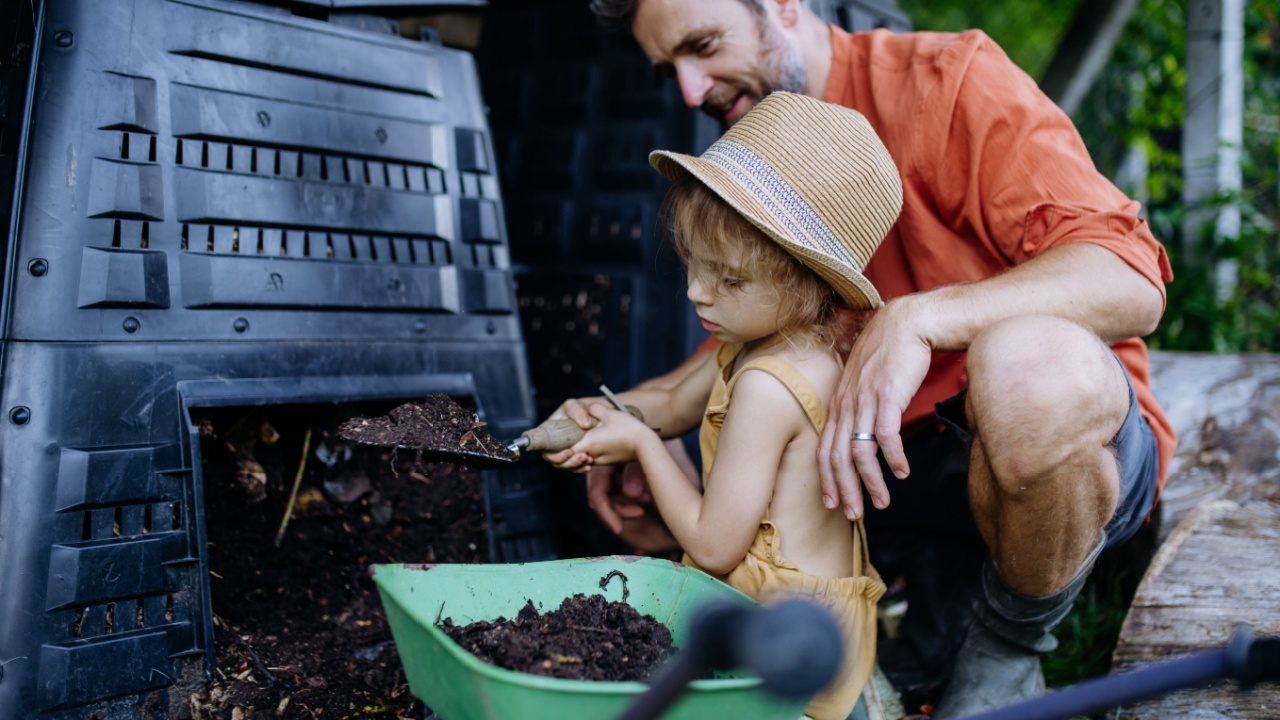 Father with his daughter putting compost out of composter, farmer lifestyle.
