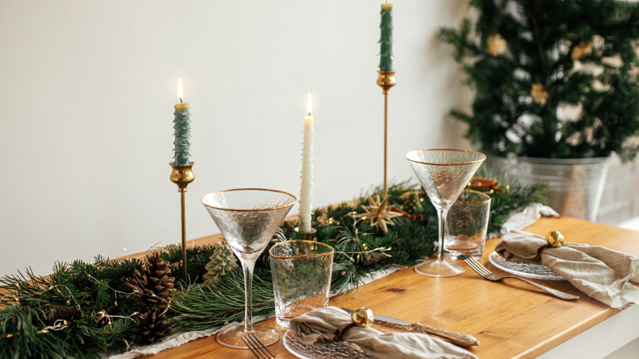 Stylish Christmas table setting. Linen napkin with bell on plate, vintage cutlery, wineglass, fir branches with golden lights, pine cones and candle on table. Atmospheric Holiday brunch