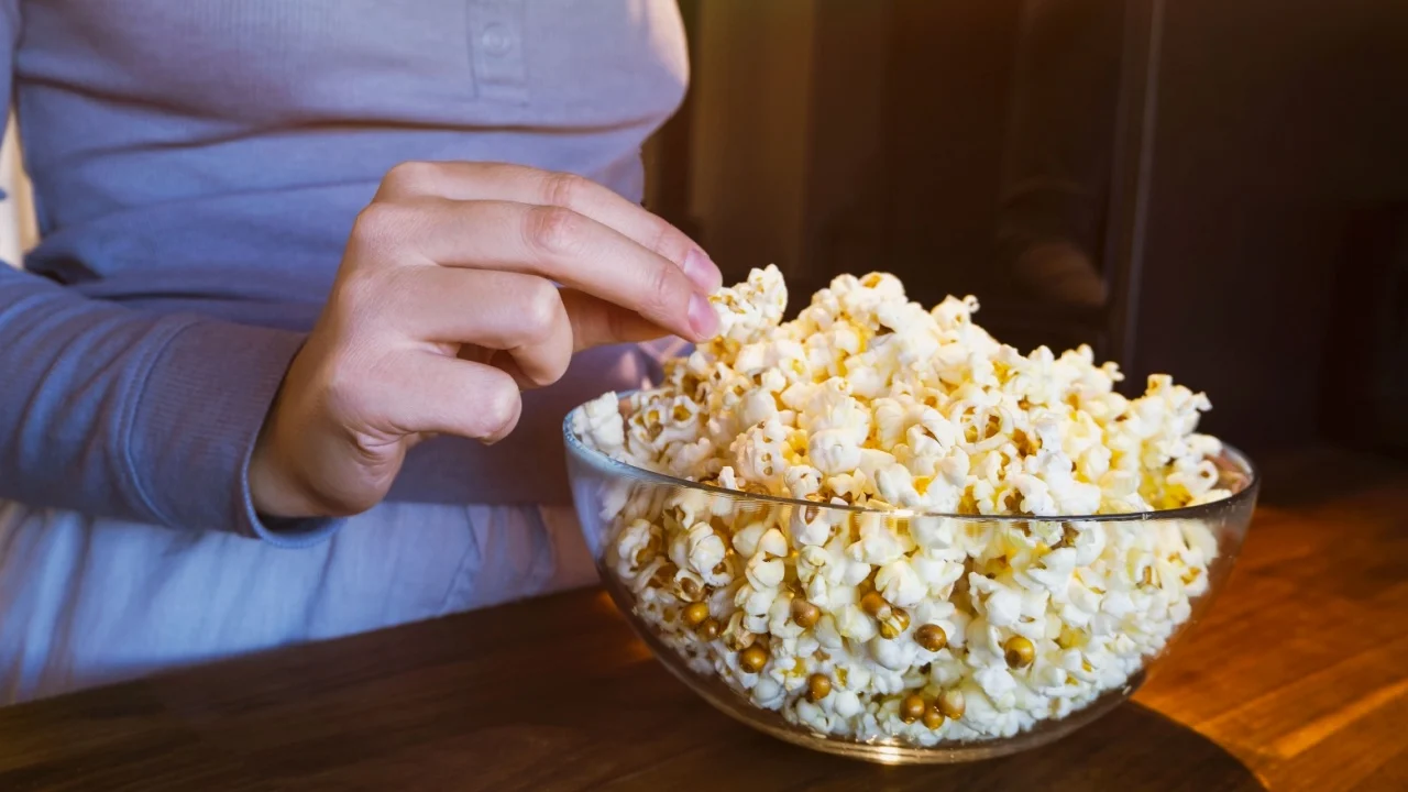 The girl reaches for the popcorn in a glass cup in the kitchen. Getting ready to watch a movie. High quality photo