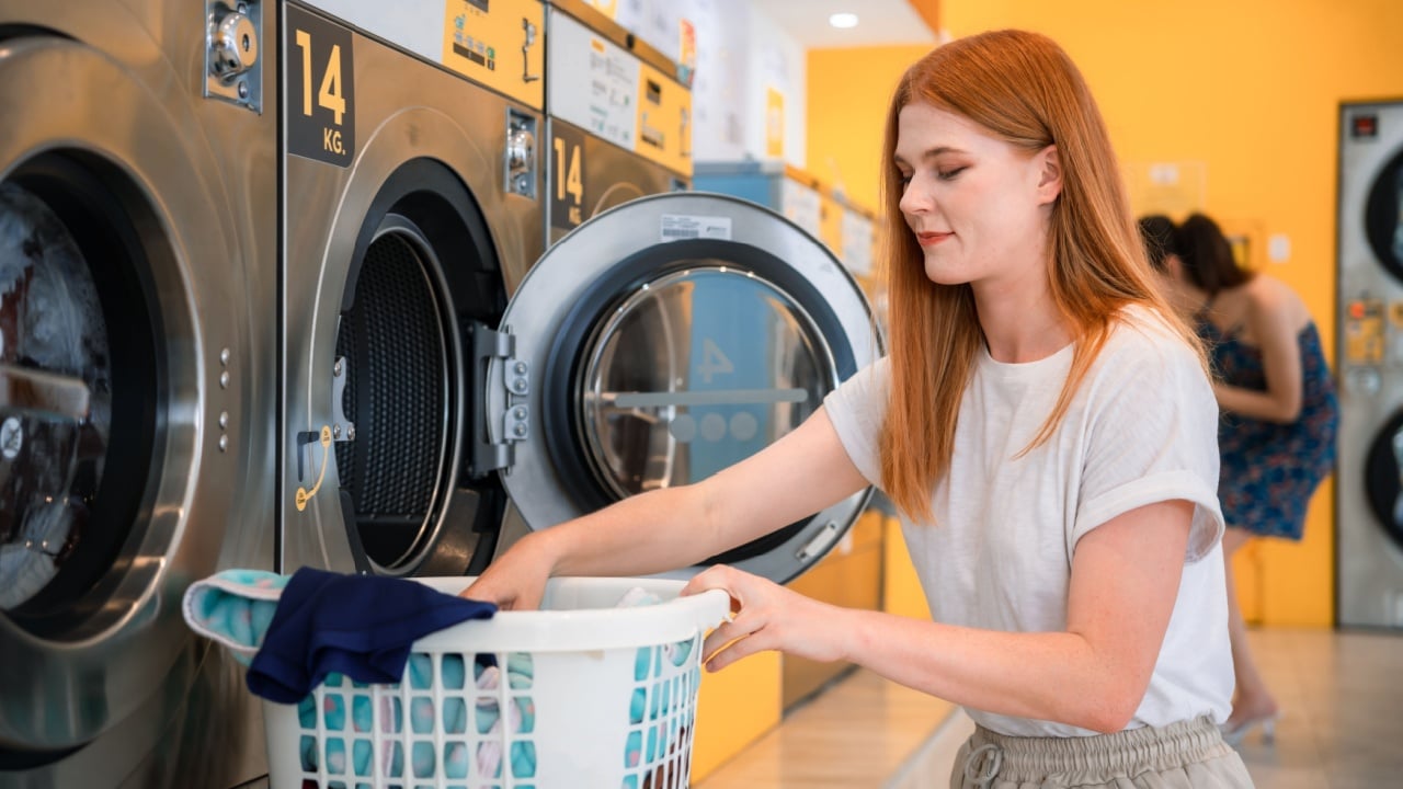 Beautiful young doing he's weekly washing in a self-service public laundry.