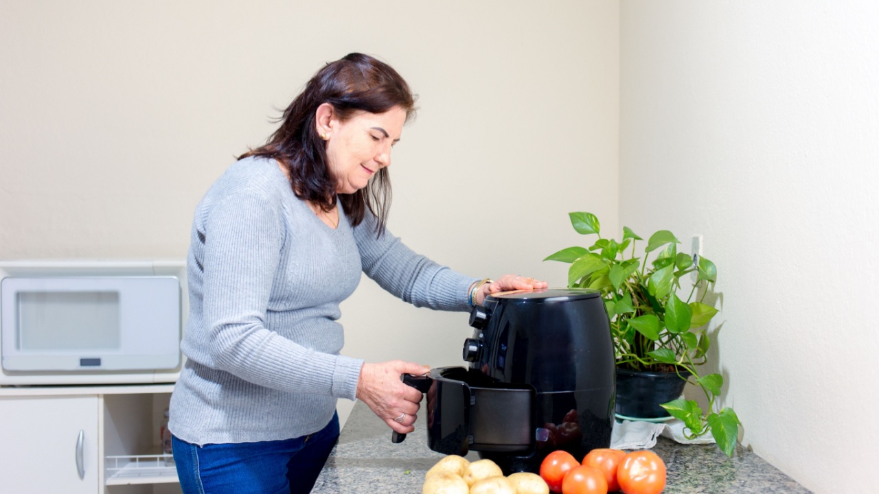 Mature woman using airfryer to fry potatoes without oil. Preparing food in an electric fryer.