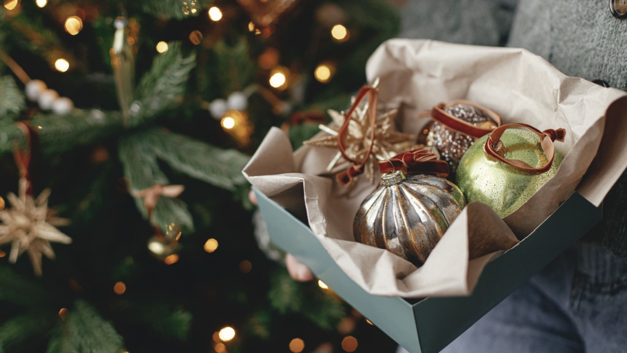 Woman in cozy sweater holding box with christmas baubles in atmospheric festive room. Decorating christmas tree with vintage ornaments. Merry Christmas! Winter holidays preparation