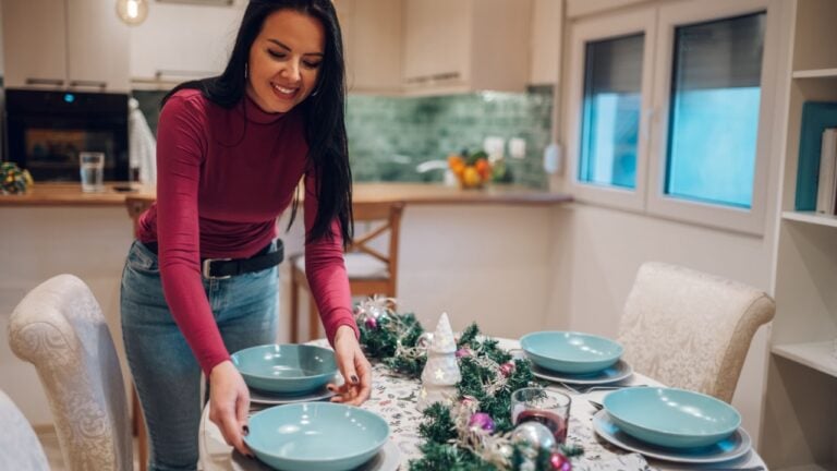 Beautiful middle aged woman decorating and setting the table for Christmas dinner. Setting the plates on the table. Female preparing for Christmas celebration in domestic interior. Copy space.