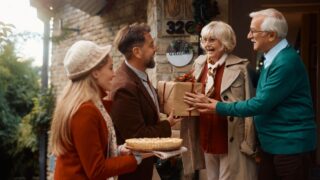 Happy man giving present to his parents while coming to visit for Christmas with his wife.