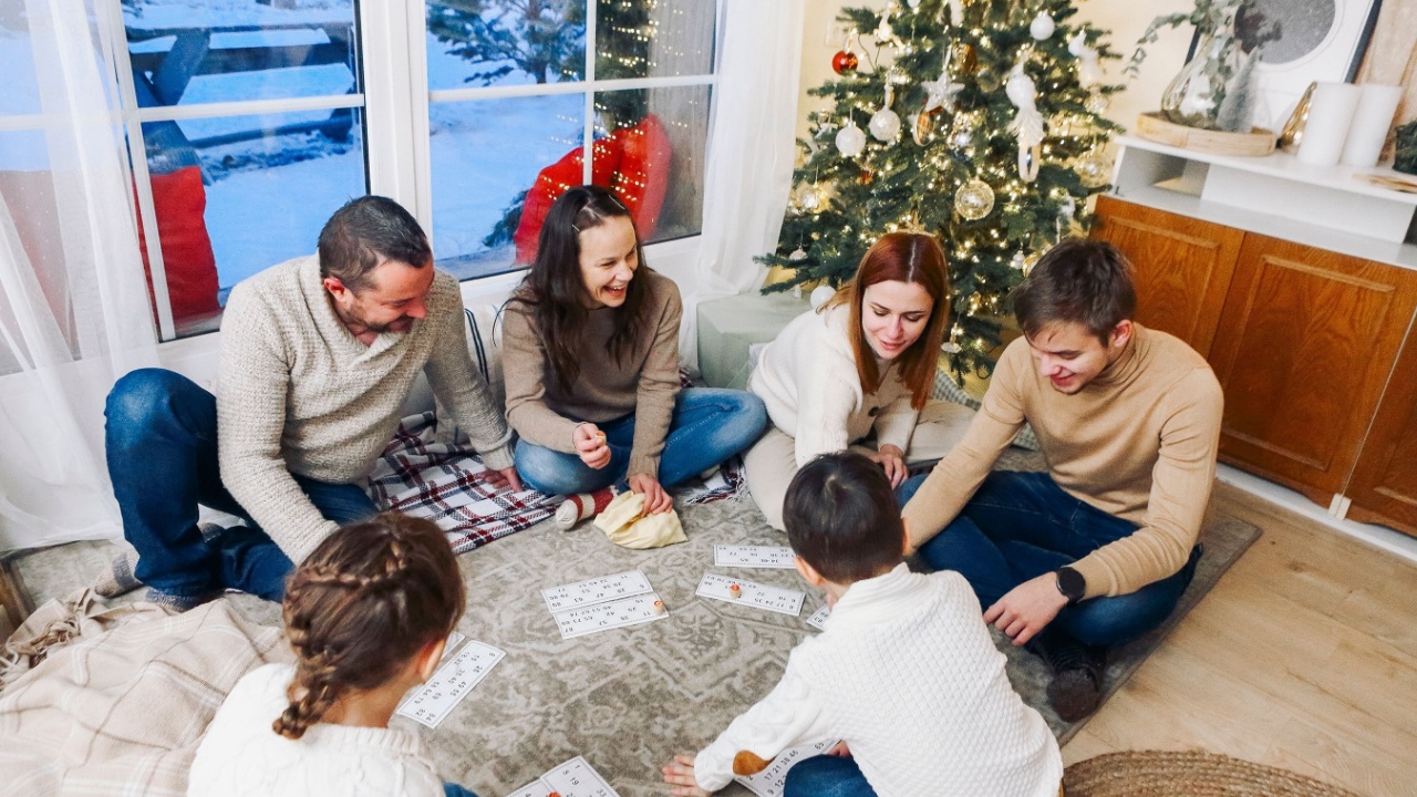 Big family with children sitting on floor near Xmas tree playing lotto board game together while spending leisure time at cozy home during Christmas holidays. Indoor winter activities