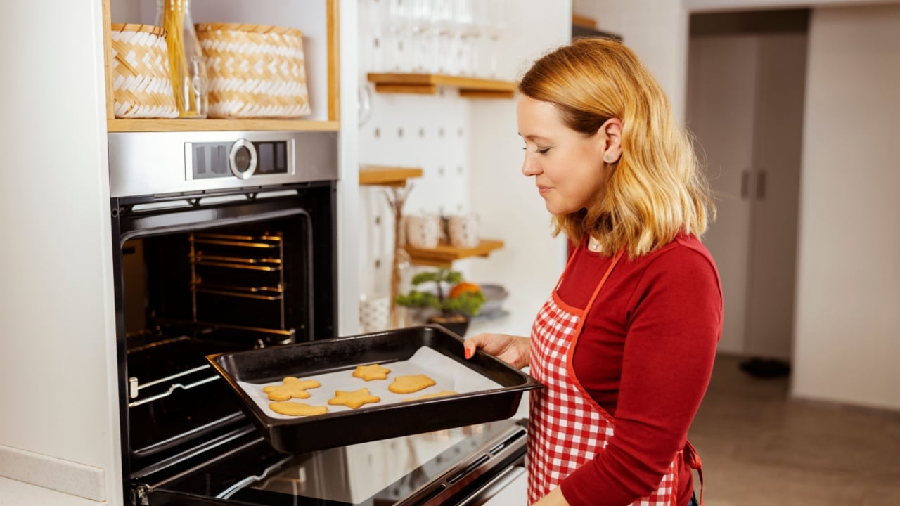 A happy woman is holding tray with delicious christmas cookies made for christmas eve.