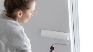 Close-up view young adult woman hand painting wall paint holding roller brush white color living room moving new home flat . Female painter decorating interior renovation residential apartment