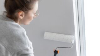 Close-up view young adult woman hand painting wall paint holding roller brush white color living room moving new home flat . Female painter decorating interior renovation residential apartment