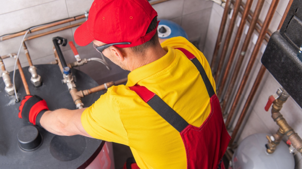 Professional Caucasian Plumber Repairing Tank Water Heater in Boiler Room of Commercial Building. Heating Equipment Maintenance Theme.