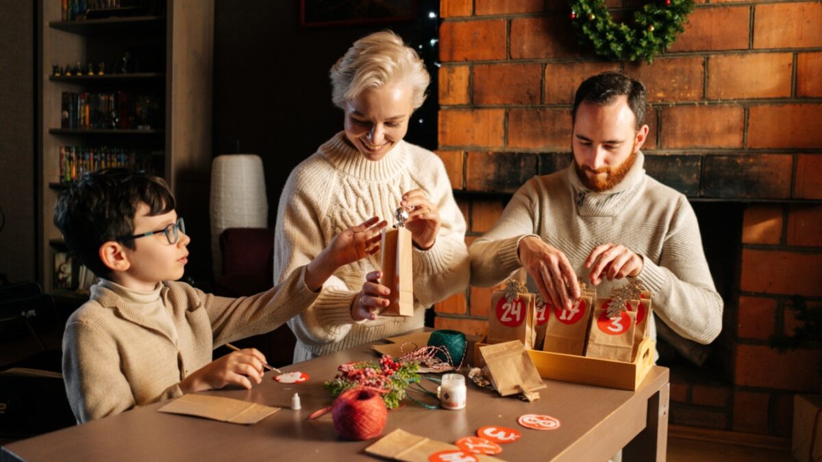 UFA, RUSSIA - 24 OCTOBER 2021. Cheerful young family making Christmas advent calendar together sitting at table on background of fireplace in cozy house on xmas Eve, enjoying togetherness preparing