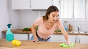 Focused woman wearing casual clothes cleaning countertop in kitchen with a rag and detergent