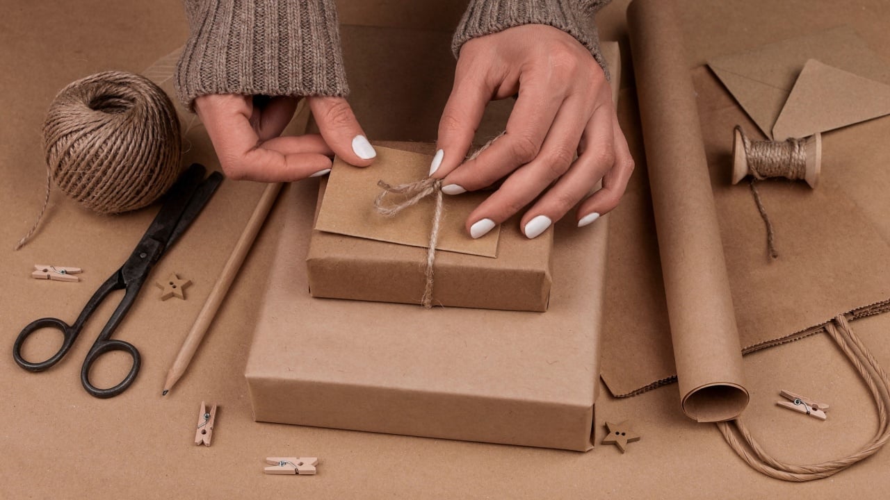 Close up woman hands packing and wrapping Christmas gift boxes in natural brown paper, high angle view