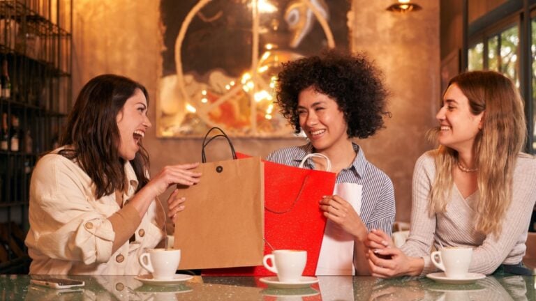 Three friends at the bar cafe giving gifts for Christmas. Friends come from shopping and check the bags in the fashion stores.
