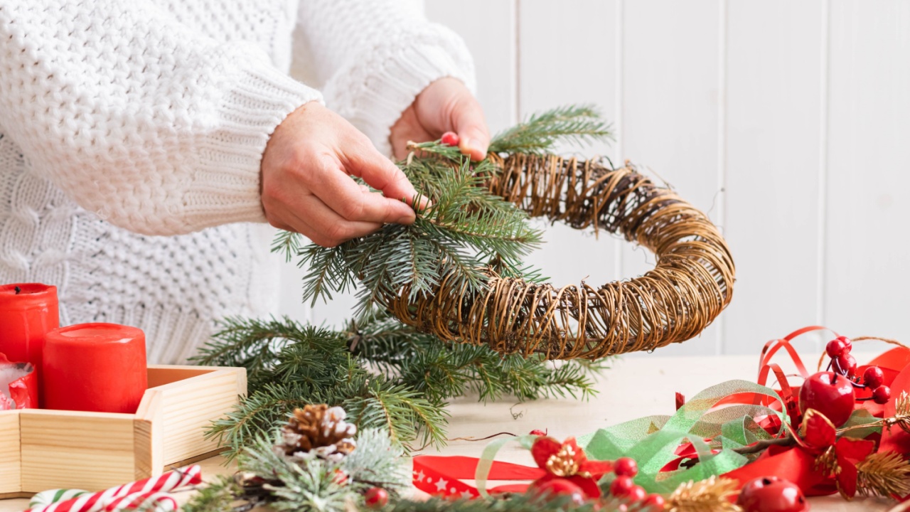 A woman makes and decorates Christmas wreath of spruce branches with red berries colorful ribbons