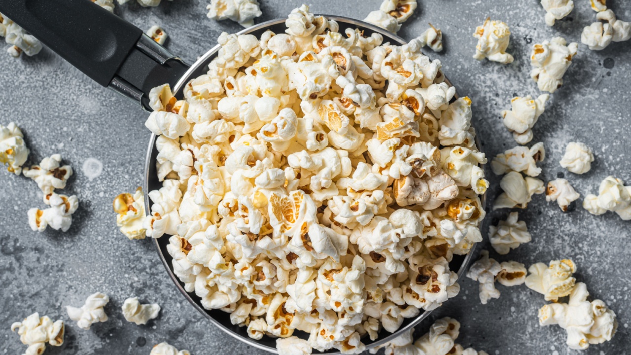 Cooking salted popcorn in a skillet. Gray background. Top view.