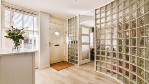 a glass block wall in a hallway with wooden flooring and white trim on the walls there is a vase full of flowers