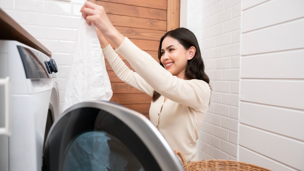 Happy Asian young woman is doing laundry in home