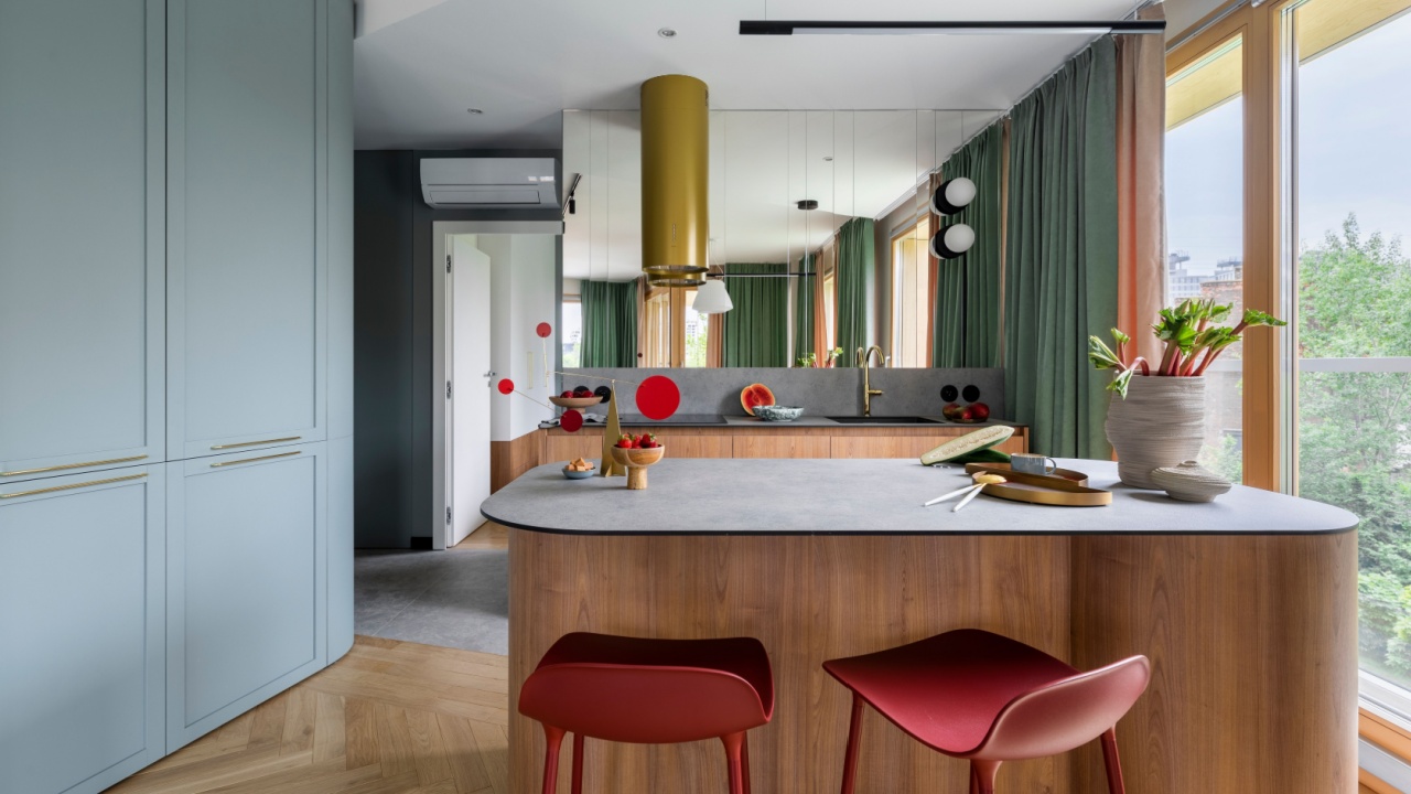Modern composition of kitchen interior with wooden kitchen island, red barstools, colorful sculpture, green curtain, gold cooker hood, vase with rhubarb and personal accessories. Home decor. Template.