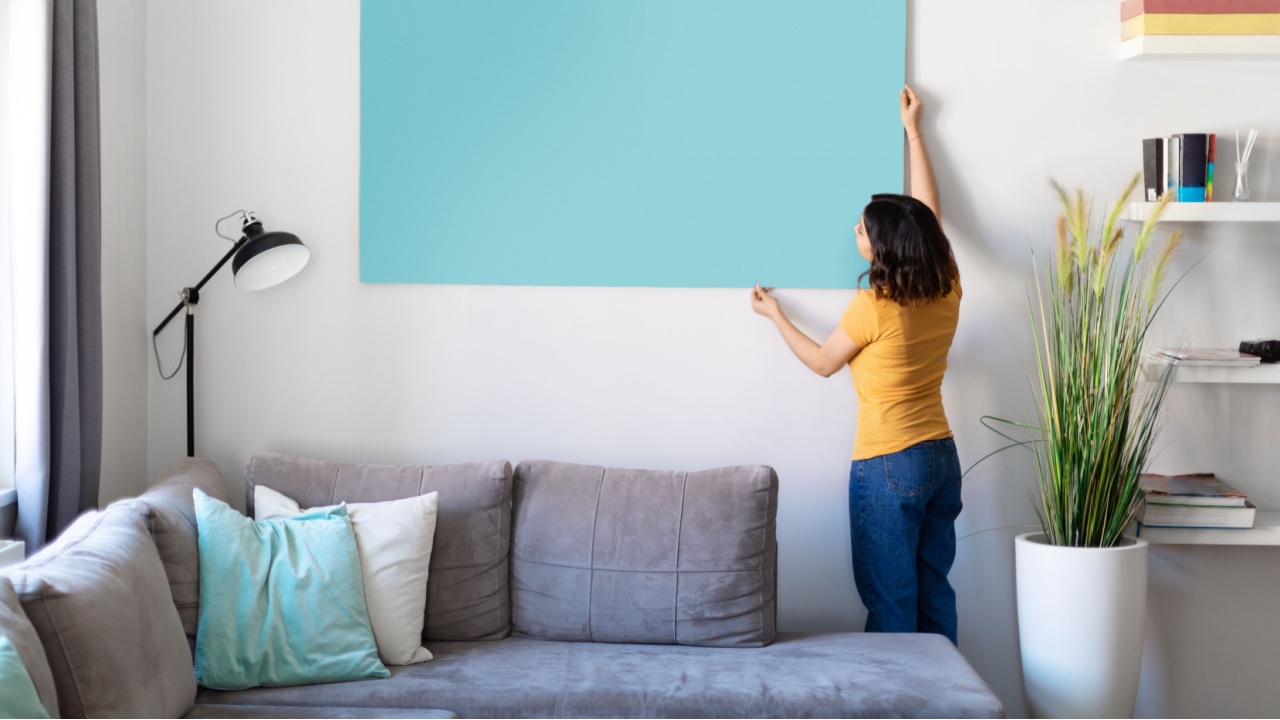 Young woman hanging large empty poster on the wall in living room at home, millennial middle eastern female decorating modern apartment with blank painting, copy space for your design, mockup