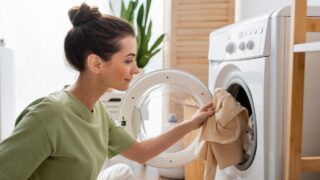 Side view of young woman putting clothes in washing machine at home