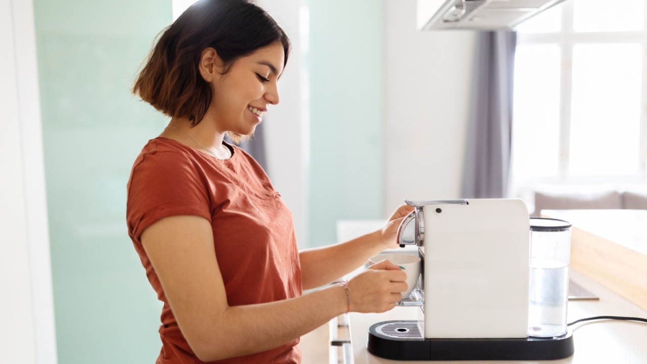 Beautiful Young Arab Woman Using Modern Coffee Machine In Kitchen, Smiling Middle Eastern Female Holding Cup And Preparing Caffeine Drink In The Morning At Home, Side View Shot With Copy Space