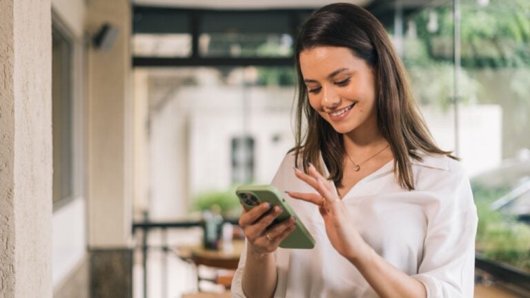 Smiling professional woman using smartphone in modern office corridor