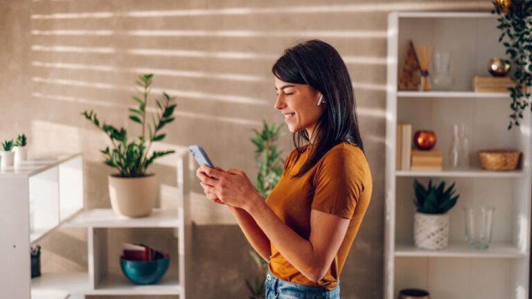 portrait of a woman using smartphone and posting good news at social media. Smiling young female enjoying online shopping or ordering in mobile phone app on the weekend.