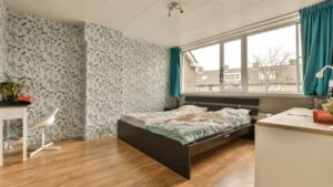 a bedroom with floral wallpaper on the walls and wood flooring in front of bed, desk and window