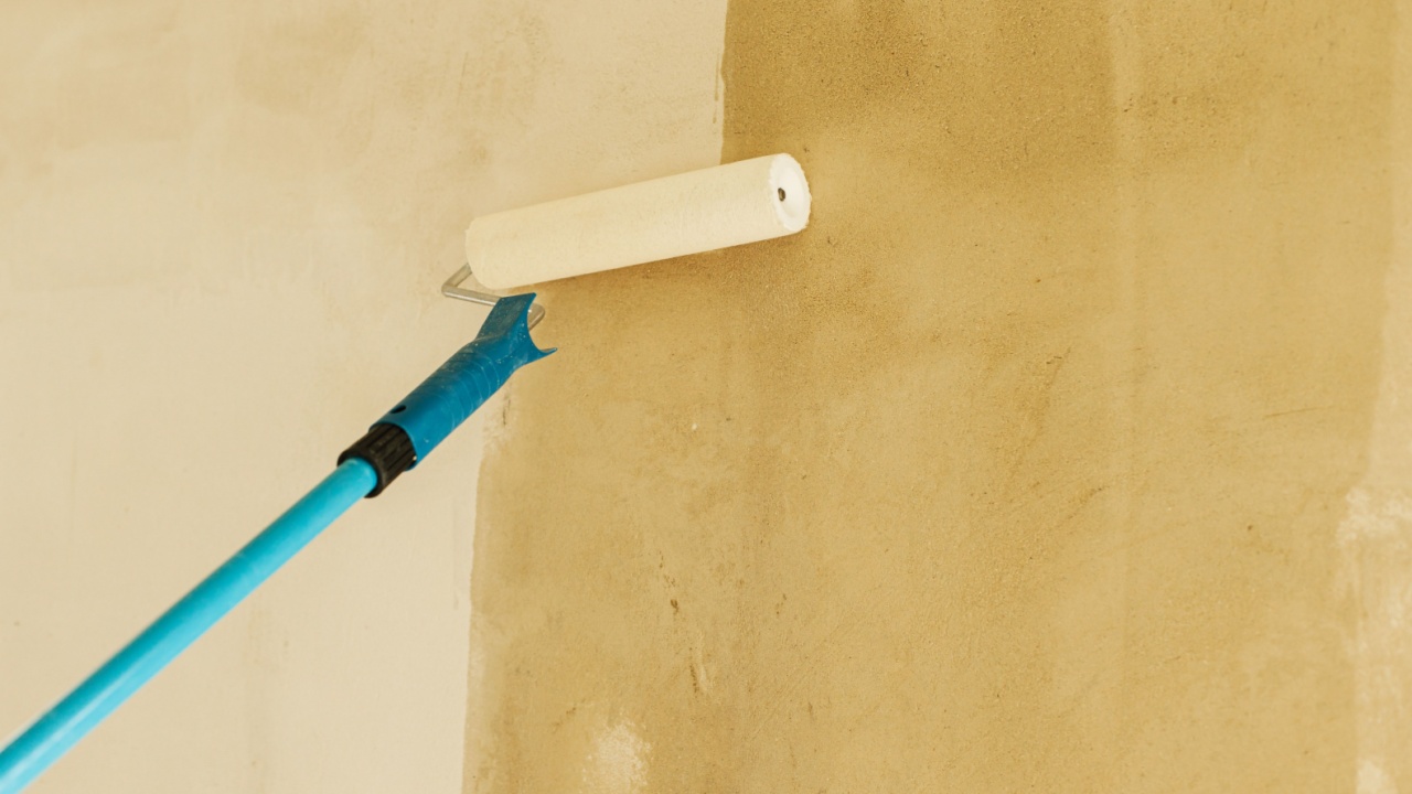 Worker priming walls in new building. Roller brush with prime covering plaster walls. Construction of house and home renovation concept.