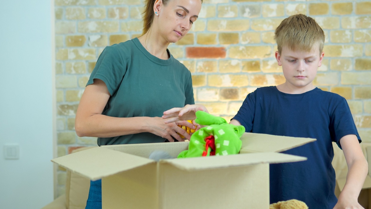 Happy volunteer woman with son separating donations toys in carton package.
