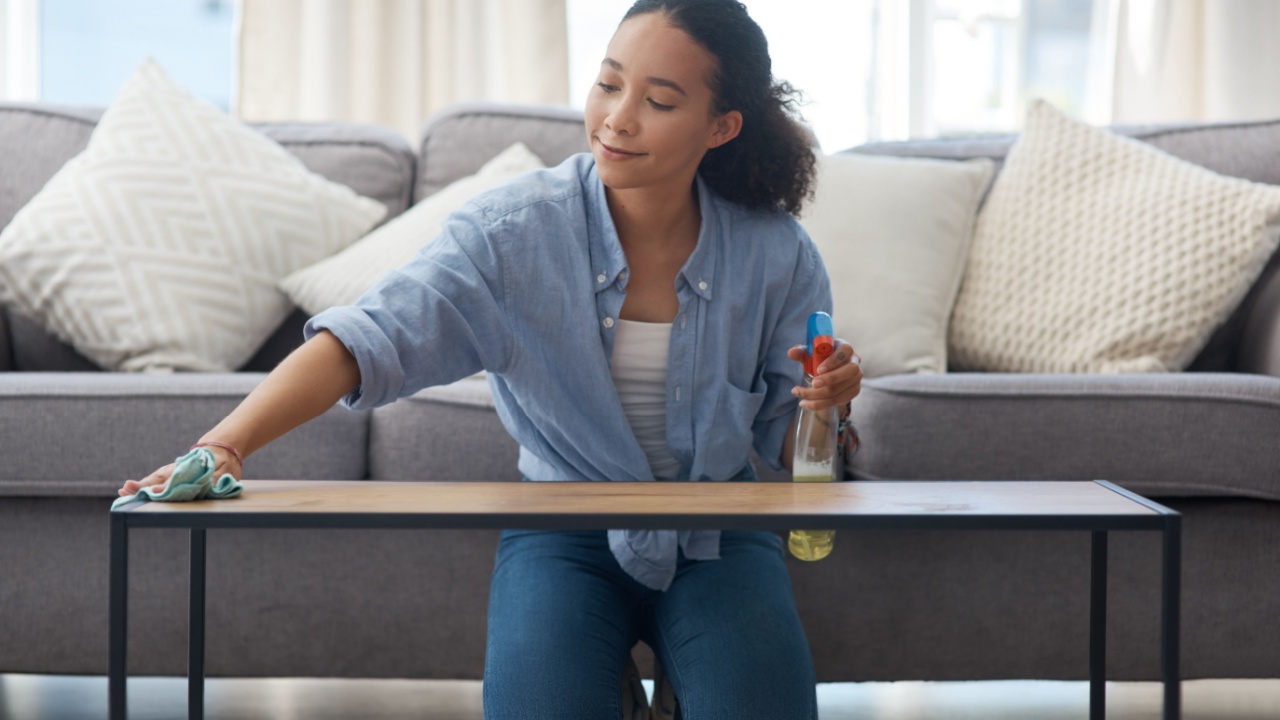 Woman, cloth and cleaning home or table with detergent for dust, bacteria or dirt in living room. Happy female person or cleaner with spray bottle or product to clean wood furniture for housekeeping