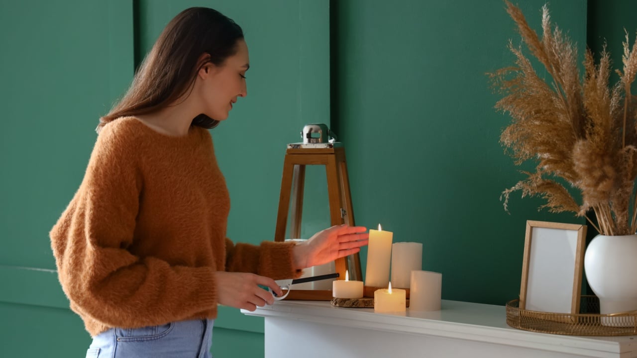 Young woman lighting candle on mantelpiece at home