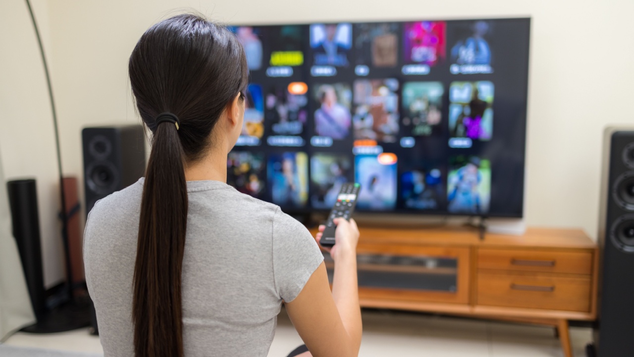 Woman watch TV and use remote control for choosing program at home