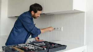 Professional electrician using screwdriver while installing new electrical socket on home kitchen
