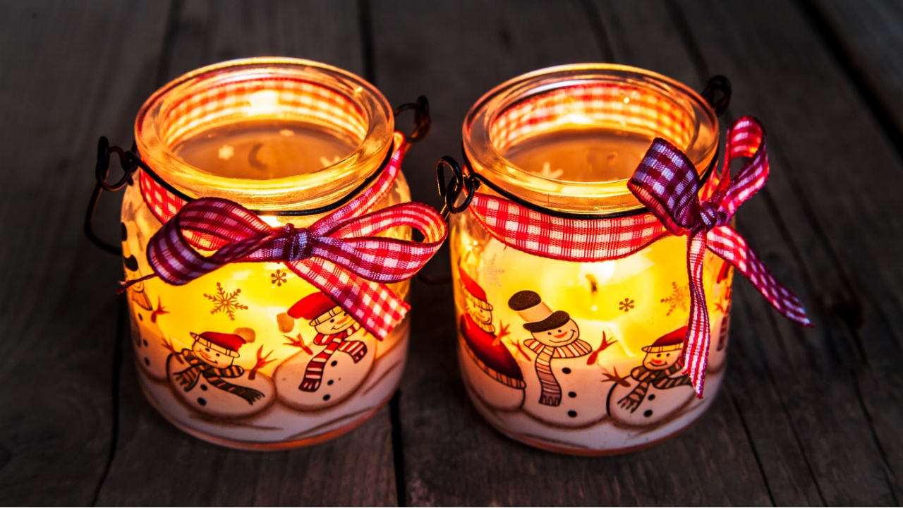 Christmas candle in a glass with drawings of snowmen and snow. Beautiful Burning festive candle tied with a ribbon on an old vintage background
