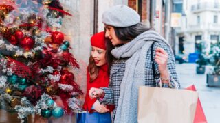 Women looking at a shop window with a christmas tree while carrying shopping bags along the street
