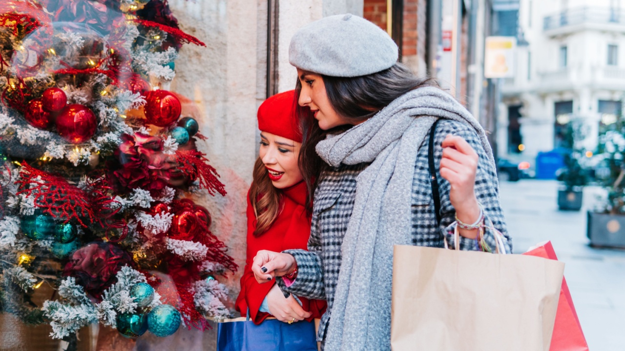 Women looking at a shop window with a christmas tree while carrying shopping bags along the street