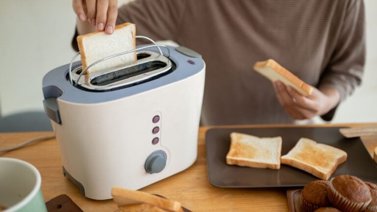 Close-up image of a beautiful young Asian woman is making tasty toasts with a toaster in the kitchen, preparing her breakfast. Cooking concept