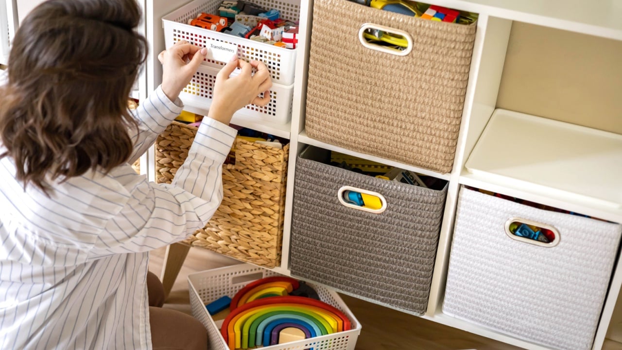 Woman mother applying paper sticker with name title on basket container clean out of childish toys comfortable storage. Female housewife organizing domestic space for kids use print mark tag