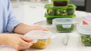 Woman sealing container with corn at white marble table in kitchen, closeup. Food storage