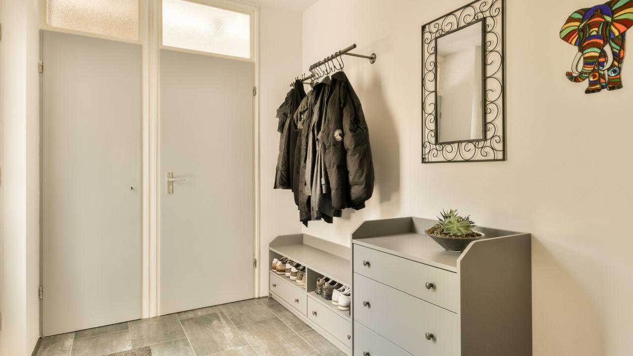a hallway with a coat rack and clothes hanging on the wall next to an entryway in a white door