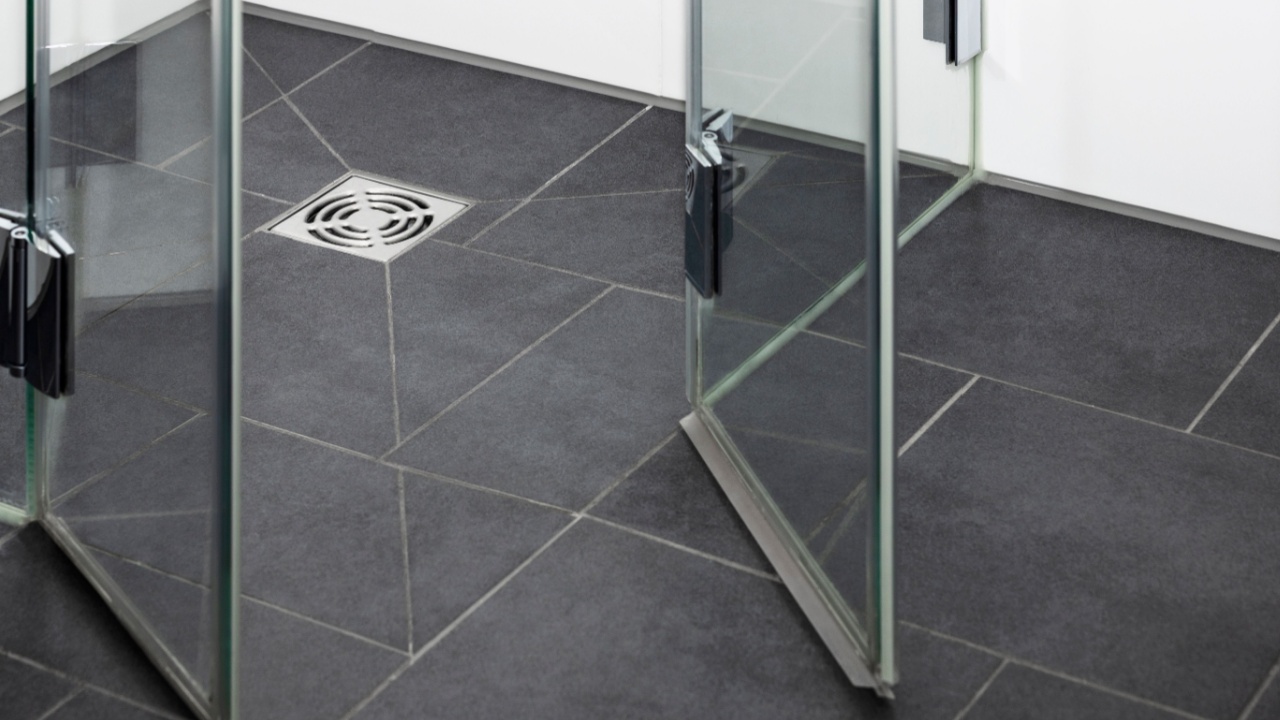 Floor Drain Metal Hole for Draining Water in Modern Shower Cabin in Bathroom with Ceramic Tiles and Glass Shower Door. Close-up.