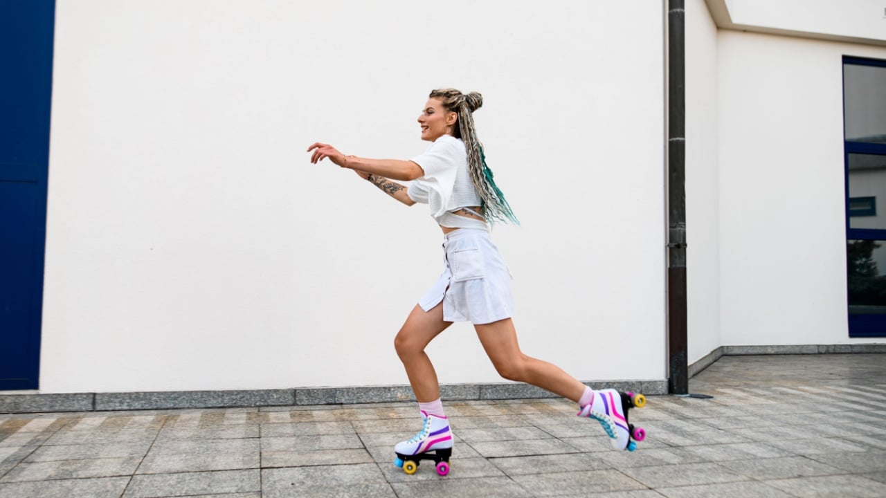 Young smoling woman with retro roller skates outside against white wall background. Healthy lifestyle. Sport activity.