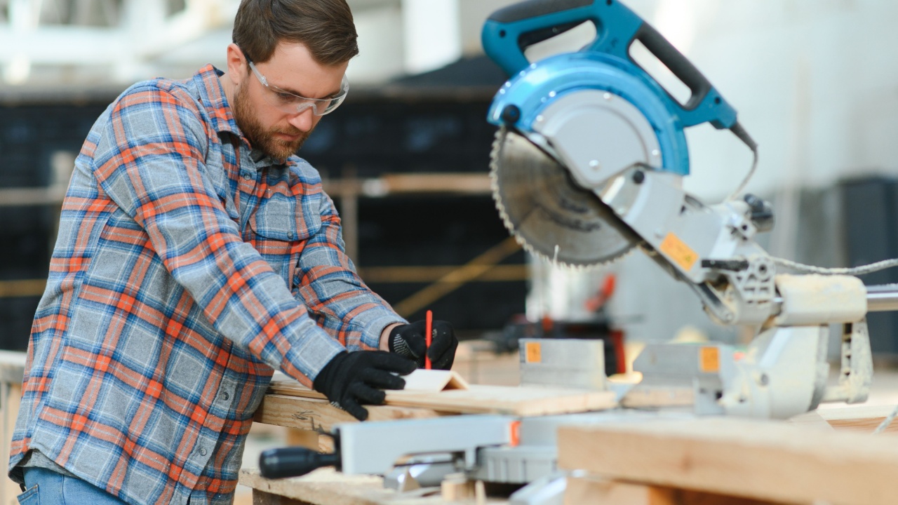 Wood cutting table with electric circular saw. Professional carpenter in uniform cutting wooden board at sawmill carpentry manufacturing . Sawing machine.
